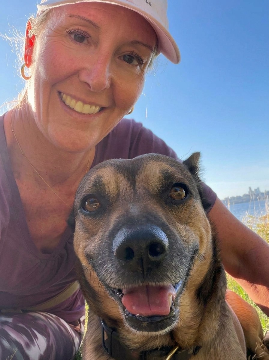 Lauren smiling outdoors with a happy dog, by the water on a sunny day