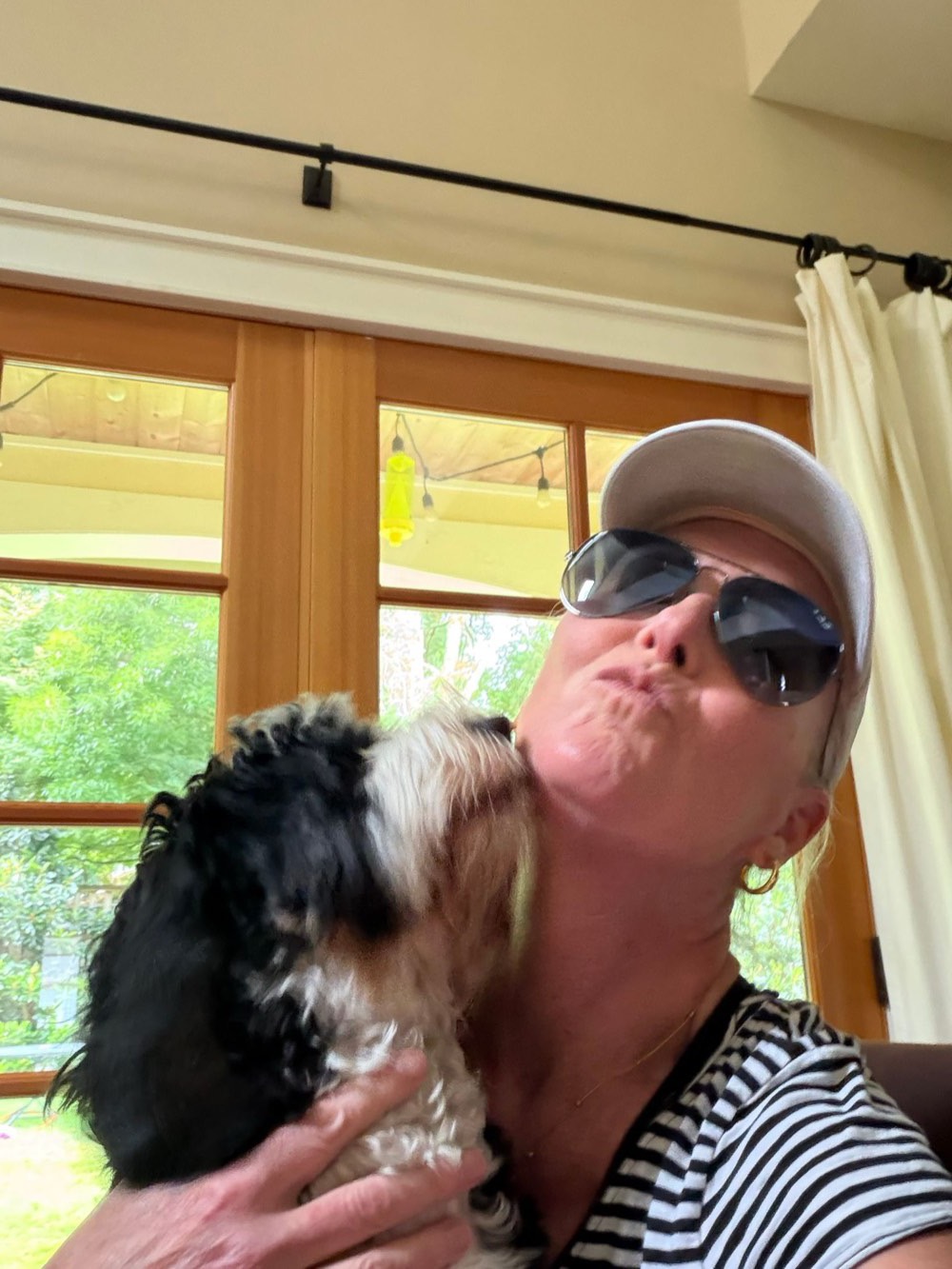 Lauren in sunglasses getting a kiss from a client's fluffy black-and-white dog